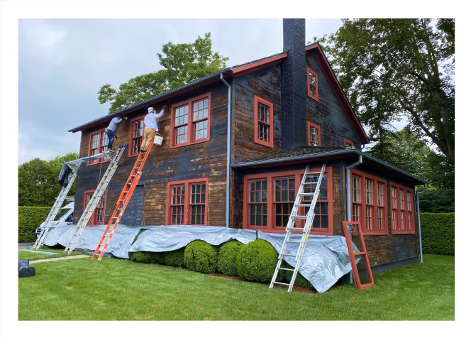 Professional painters restoring a traditional Long Island home – ladders, prep work, and protective coverings applied before final coat