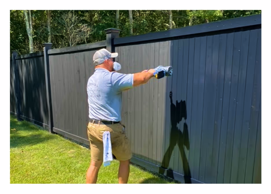 Painter applying fresh dark coat to a residential fence during an exterior restoration project in Long Island