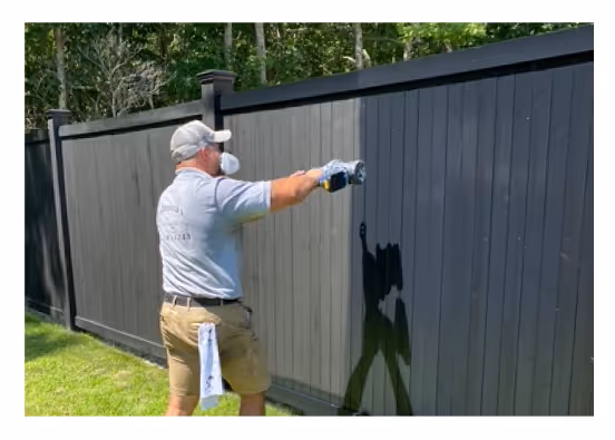 Painter applying dark protective paint to a backyard fence using spray equipment in Long Island
